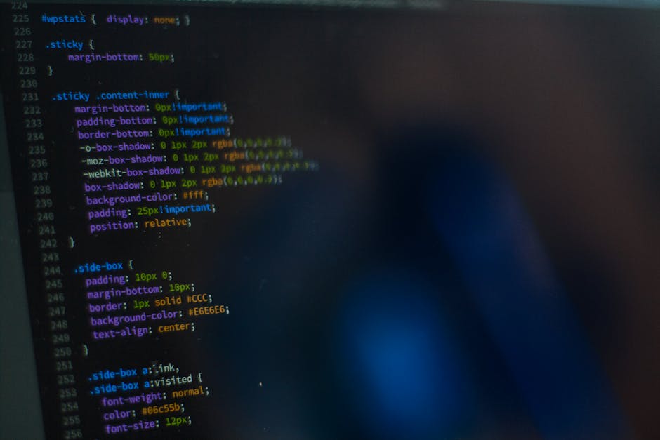 A close-up view of a computer screen displaying lines of colorful HTML code, with various CSS properties such as padding, border, background-color, and box-shadow visible. In the background, a person’