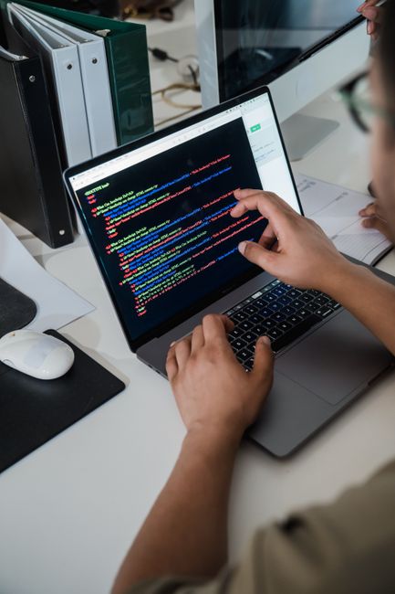 A close-up view of a computer screen displaying lines of colorful HTML code, with various CSS properties such as padding, border, background-color, and box-shadow visible. In the background, a person’